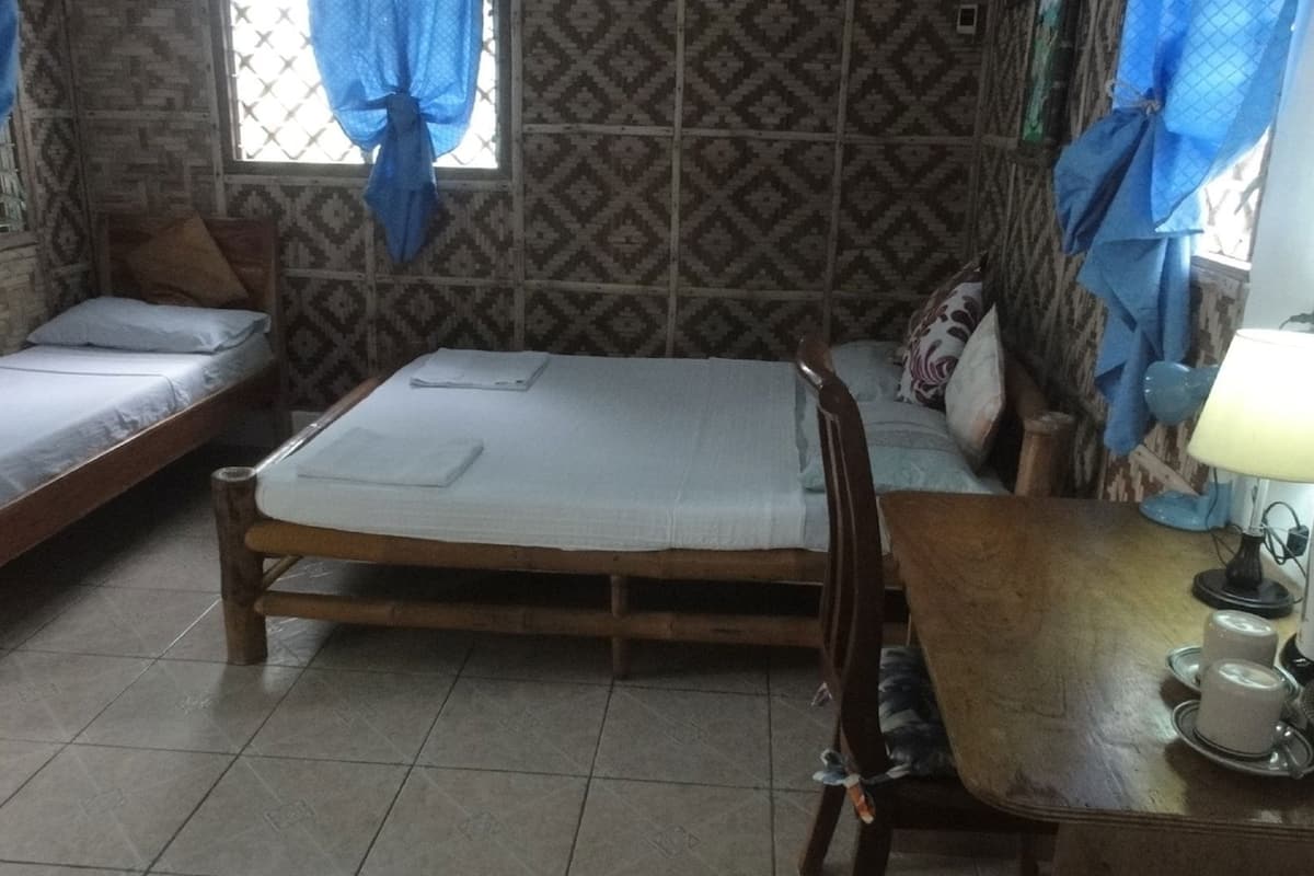 A room with two single beds, a wooden table with a kettle and cups, and patterned walls.