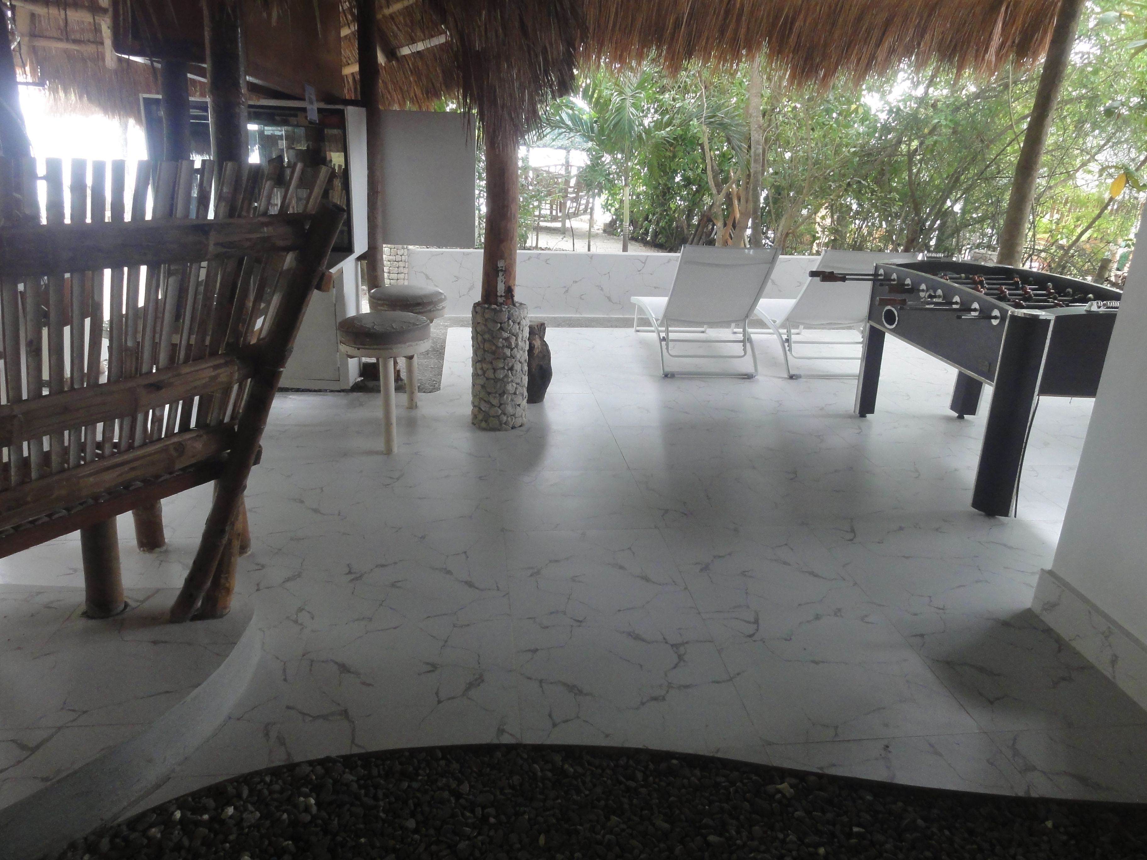 A room with a thatched roof, white marble flooring, a foosball table, and lounge chairs.
