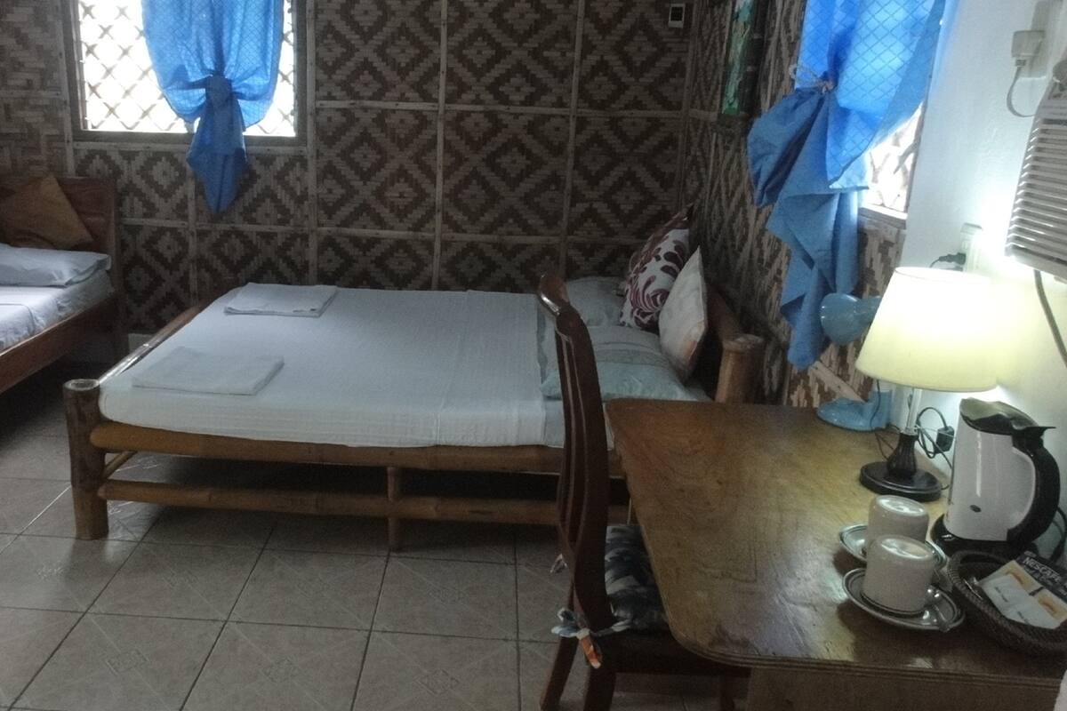 A room with two single beds, a wooden table with a kettle and cups, and patterned walls.