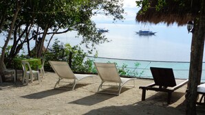 A beach with lounge chairs and a table, overlooking calm waters with boats. - Sea Turtle House (Moalboal)
