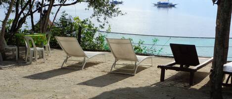 A beach with lounge chairs and a table, overlooking calm waters with boats.