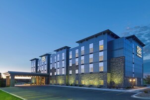 Un hotel de varios pisos con un diseño moderno, que presenta fachada de piedra y un cielo despejado al fondo.