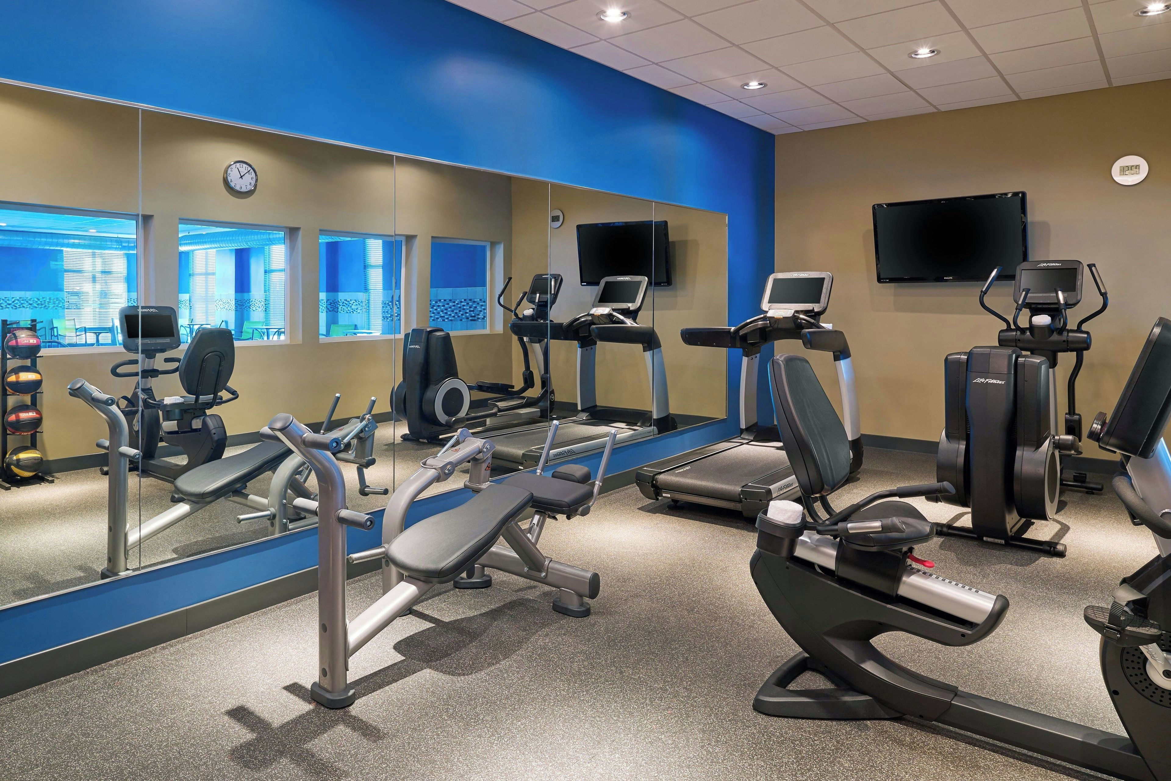 Un gimnasio con máquinas de cardio, máquinas de pesas y un espejo grande.