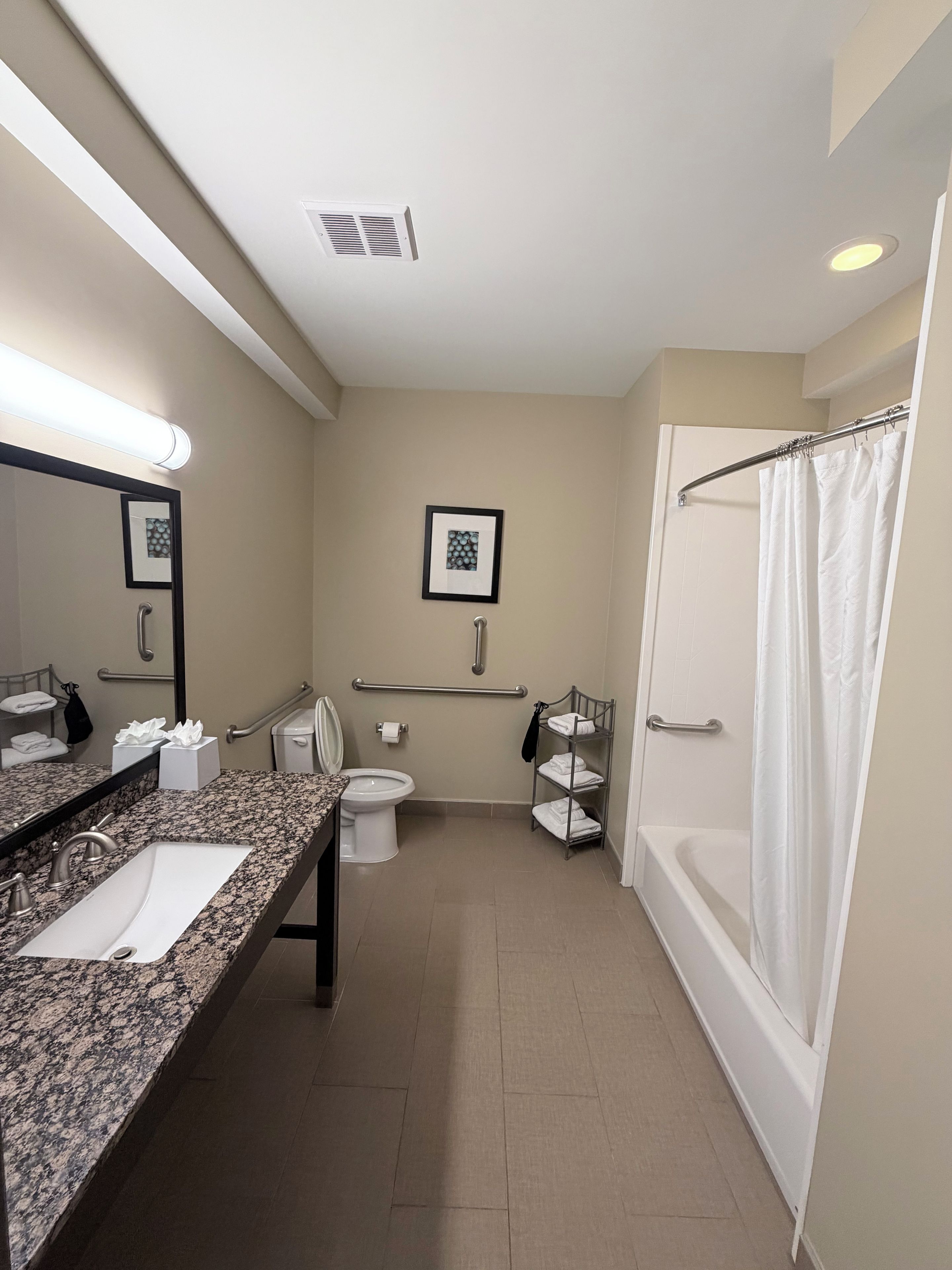 A modern bathroom with a granite countertop sink, a toilet, a bathtub, and a shower curtain.