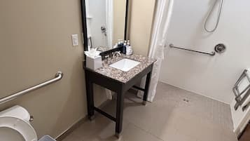 A bathroom with a toilet, sink, mirror, shower, and grab bars.