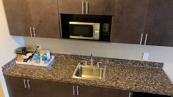 A kitchen with a granite countertop, stainless steel sink, and a microwave above the cabinets.
