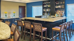 Zona de bar con encimera de granito, taburetes y estantería de botellas de licor.