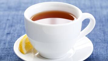A white cup of tea on a saucer with a lemon slice beside it, placed on a blue textured surface.