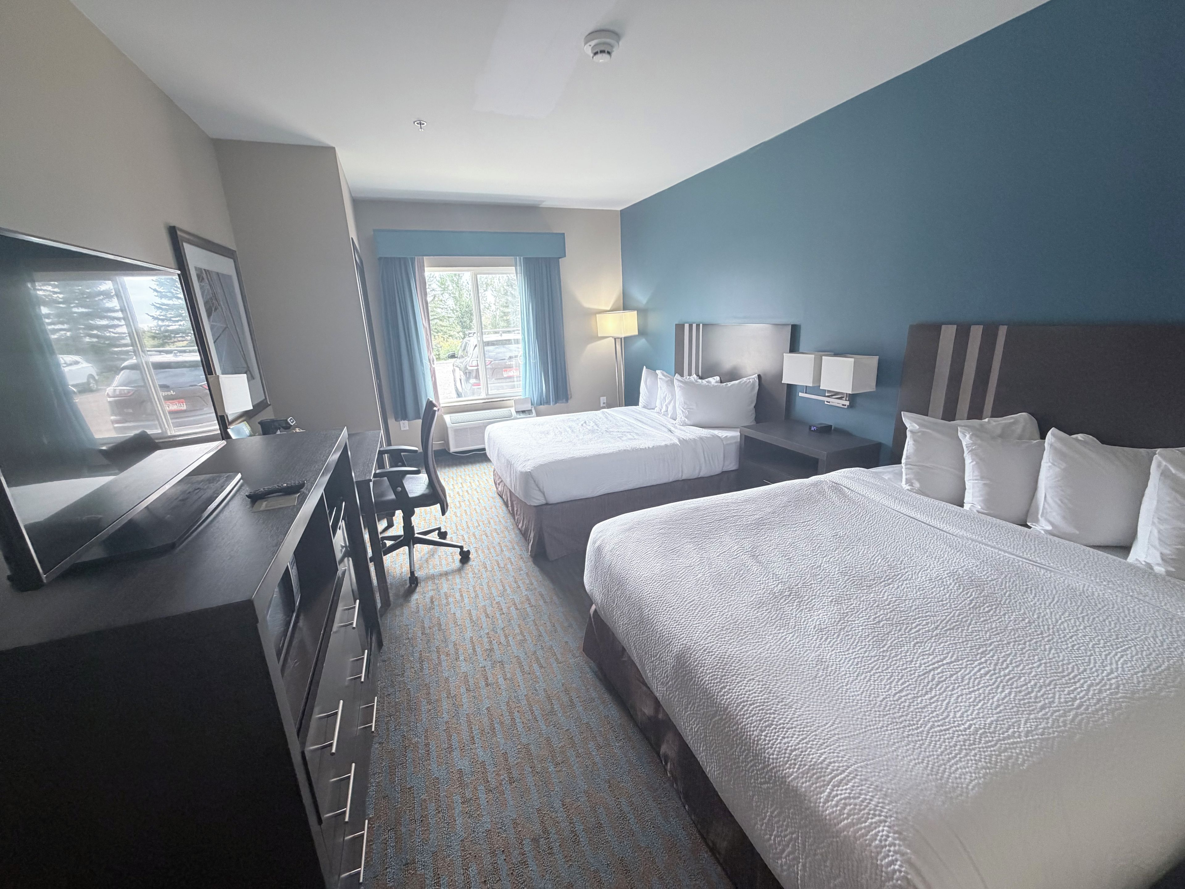 Een hotelkamer met twee bedden, een bureau met een computer, een televisie en een raam met gordijnen.