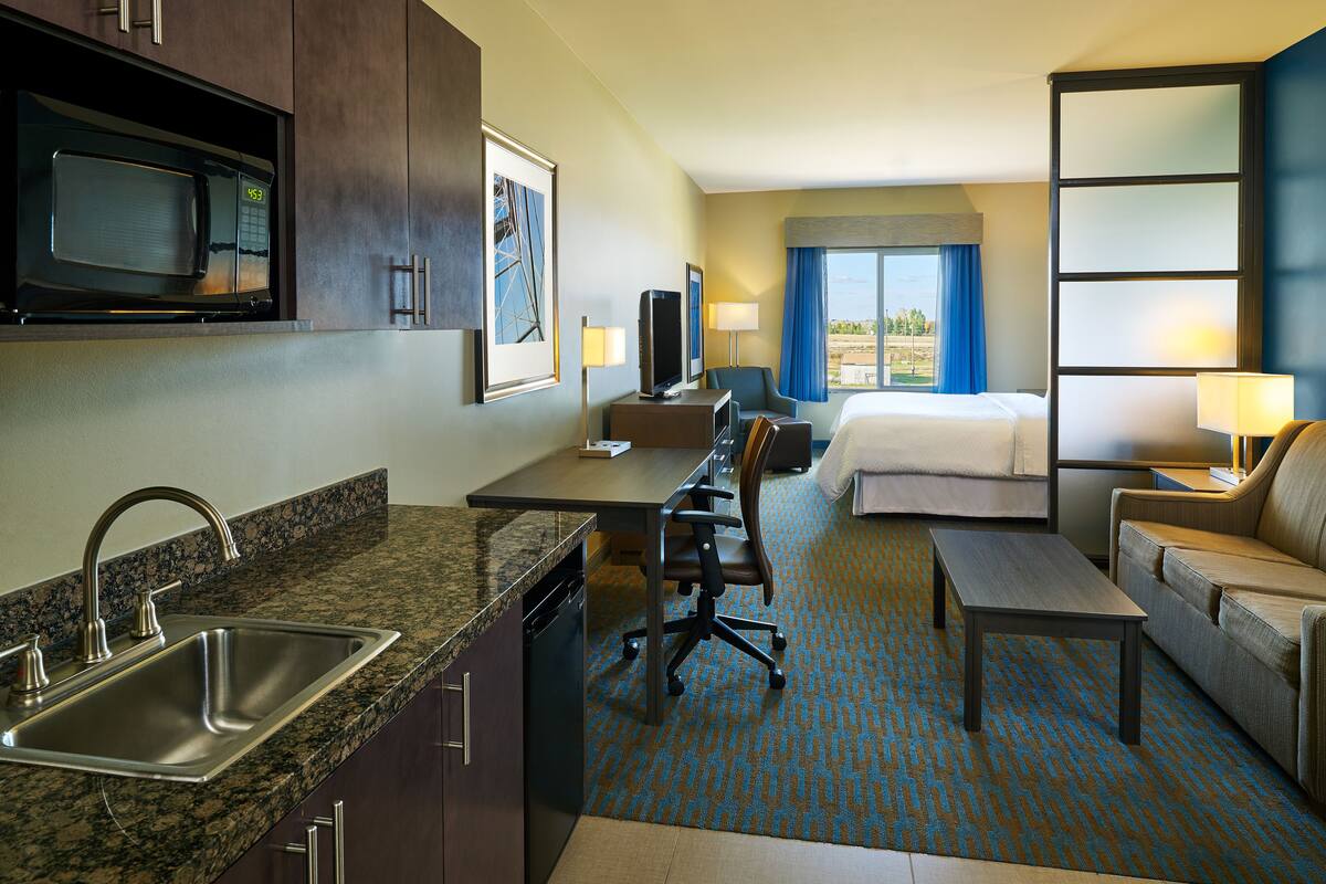 Quarto de hotel com cozinha compacta, cama, escrivaninha, cadeira e sofá.