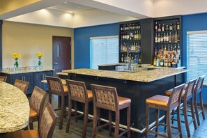 A bar area with a granite countertop, bar stools, and a variety of liquor bottles. - Four Points by Sheraton Williston (Williston)