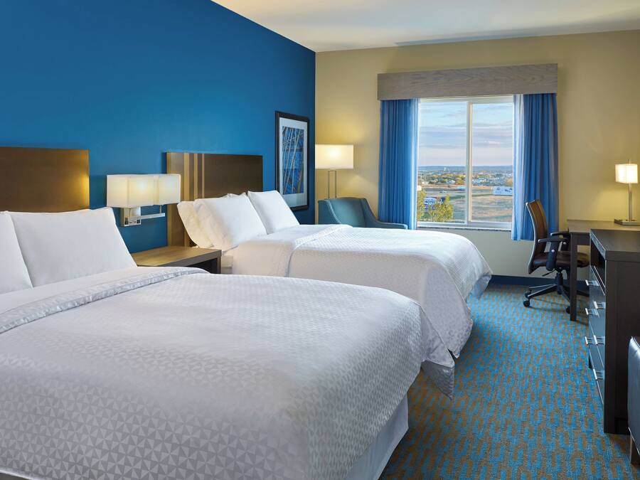 A hotel room with two beds, a desk, a chair, a TV, and a window with a view.