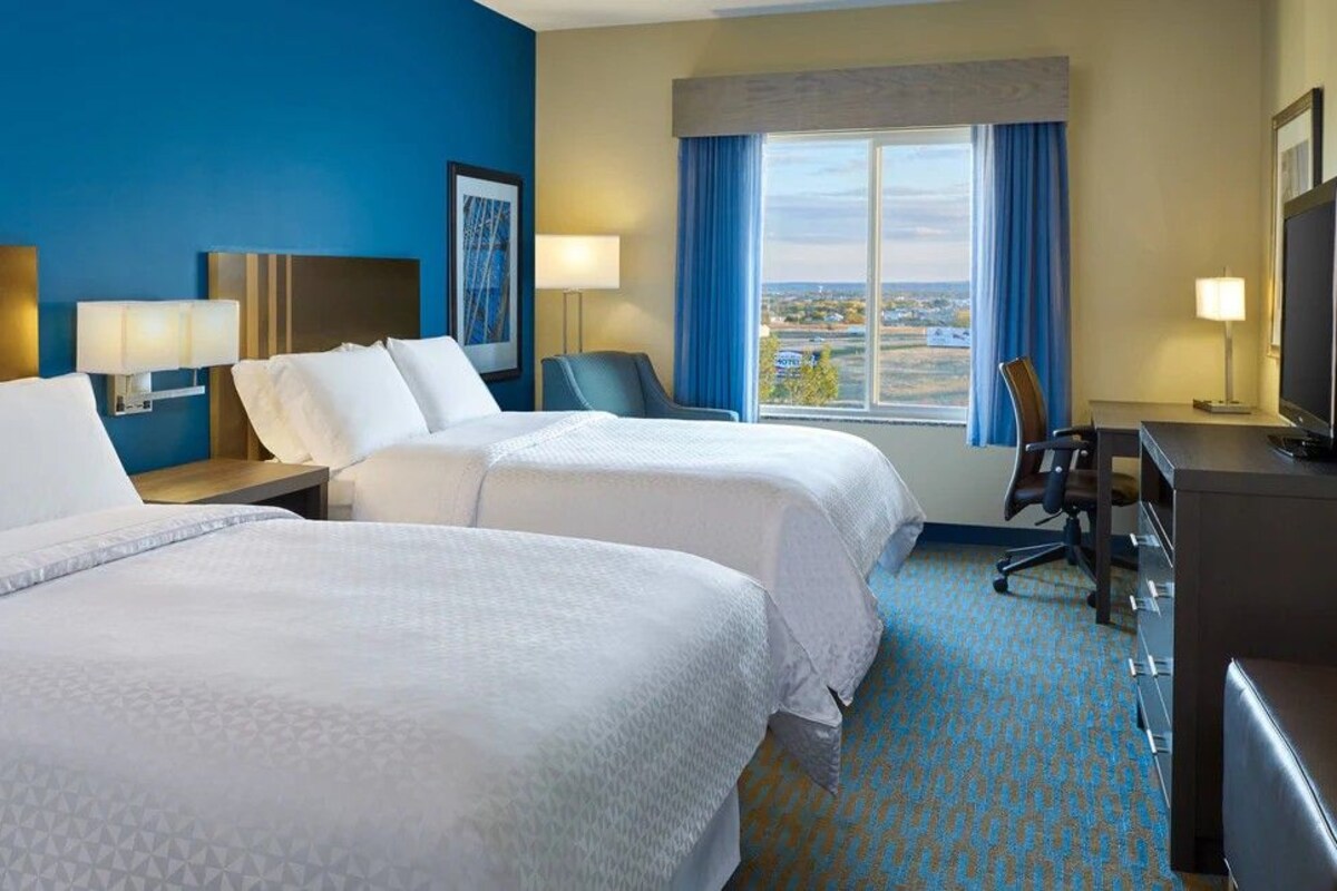A hotel room with two beds, a desk, a chair, and a television.