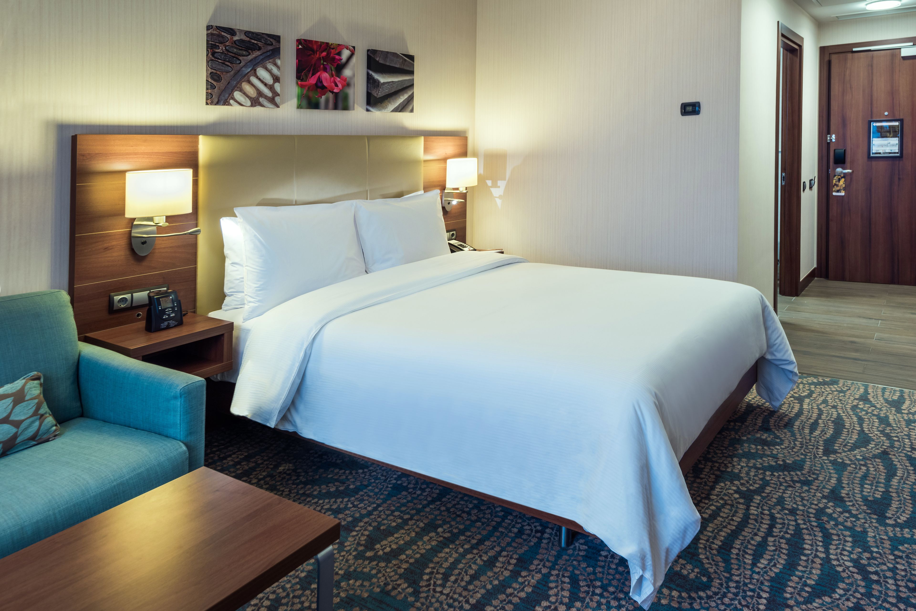 A hotel room with a large bed, a sofa, a nightstand with a lamp, and a wall-mounted TV.