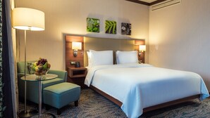 A hotel room with a bed, a desk with a lamp, a chair, and a small table with fruit. - Hilton Garden Inn Astana (Astana)