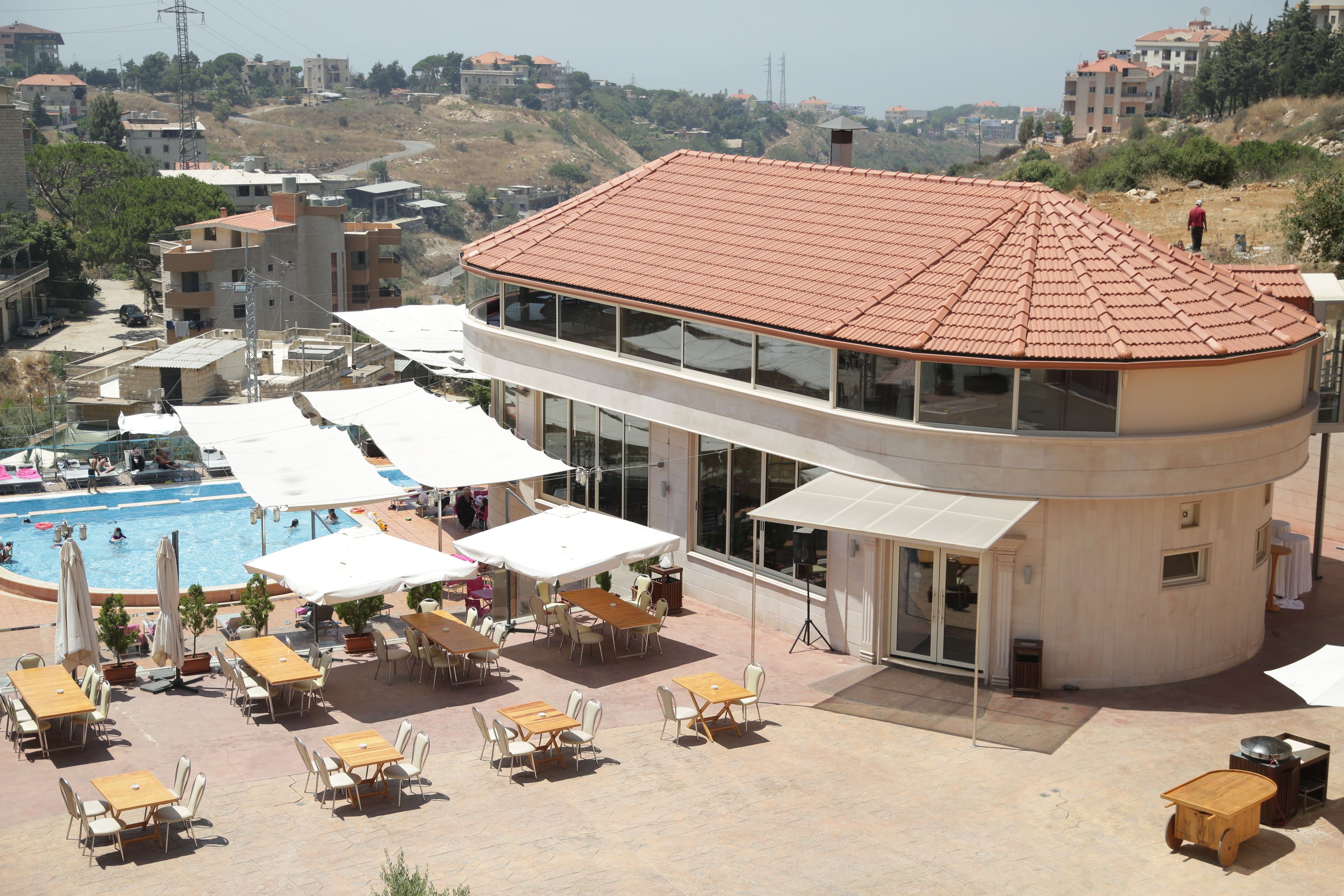 Un edifici modern amb un teulat corbat i grans finestres. Disposa d'una zona de piscina exterior amb gandules i ombrelles.