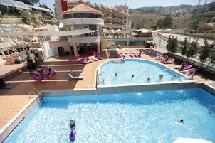 Una piscina con sillas de descanso y sombrillas, rodeada por un edificio con varios balcones.