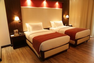 Habitación de hotel con dos camas, suelo de madera y un cabecero grande.