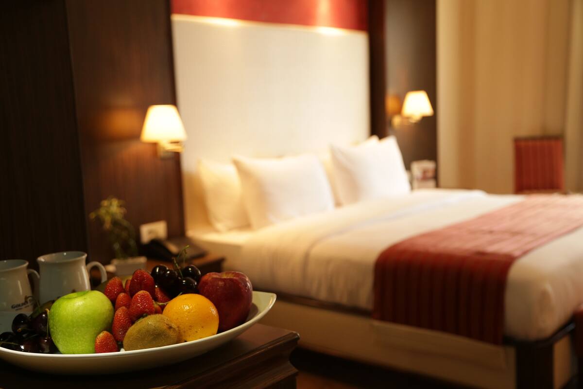 A hotel room with a bed, bedside lamps, and a fruit bowl on a nightstand.