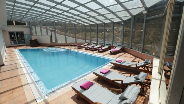 A covered swimming pool with lounge chairs and a view of the surrounding landscape. - Golden Lili Resort & Spa (Aley)