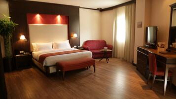 Habitación de hotel con una cama grande, un escritorio con silla, un televisor y una mesita de noche con lámpara.