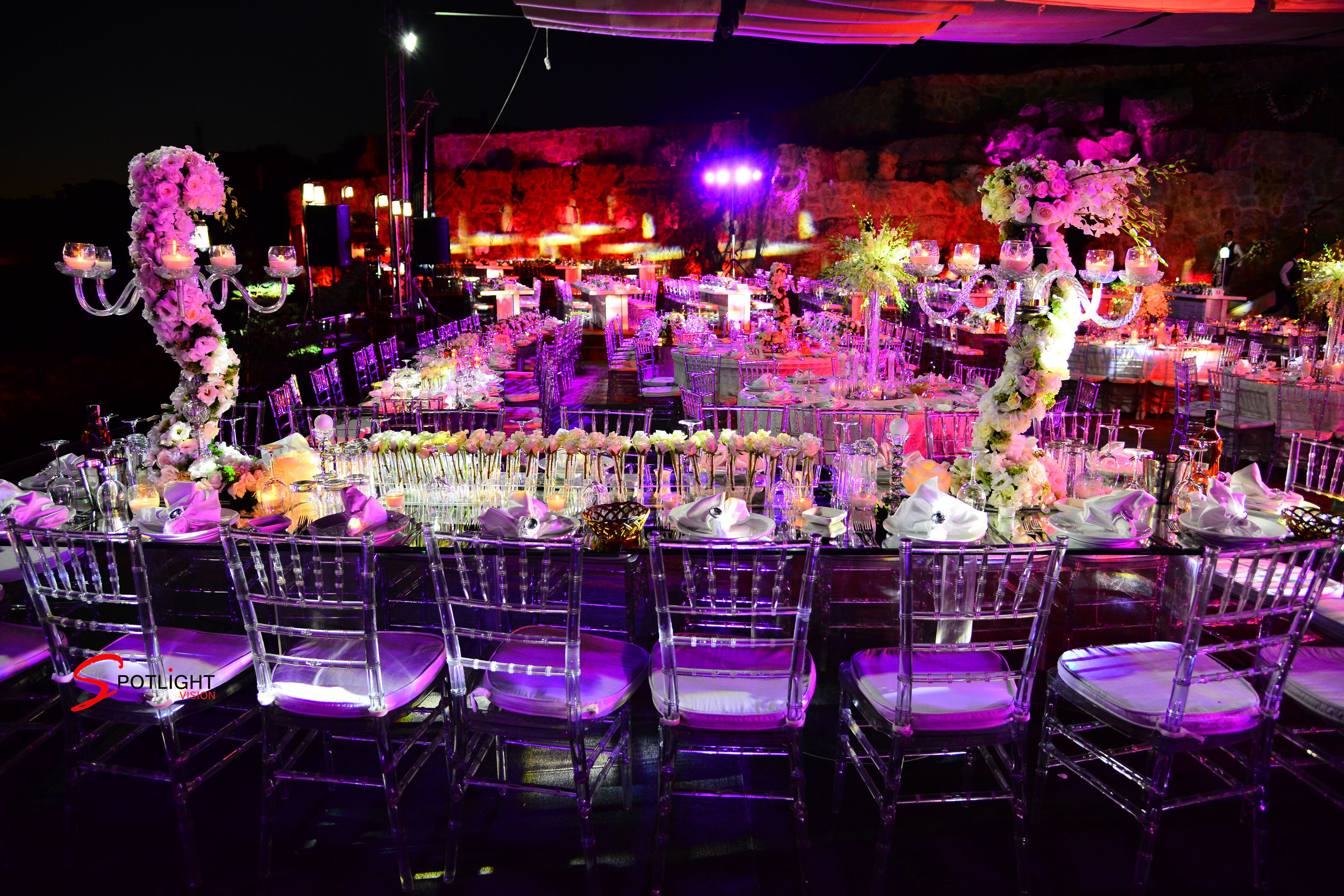 Montaje formal para un evento con mesas redondas, sillas transparentes y centros de mesa con flores.