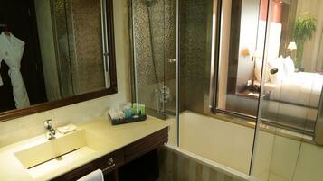 Un baño con un espejo grande, un lavamanos, una ducha y vista a un dormitorio a través de una puerta de vidrio.