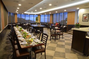 Uma ampla área de refeições com várias mesas dispostas para refeições, grandes janelas com vista e um design de teto moderno.