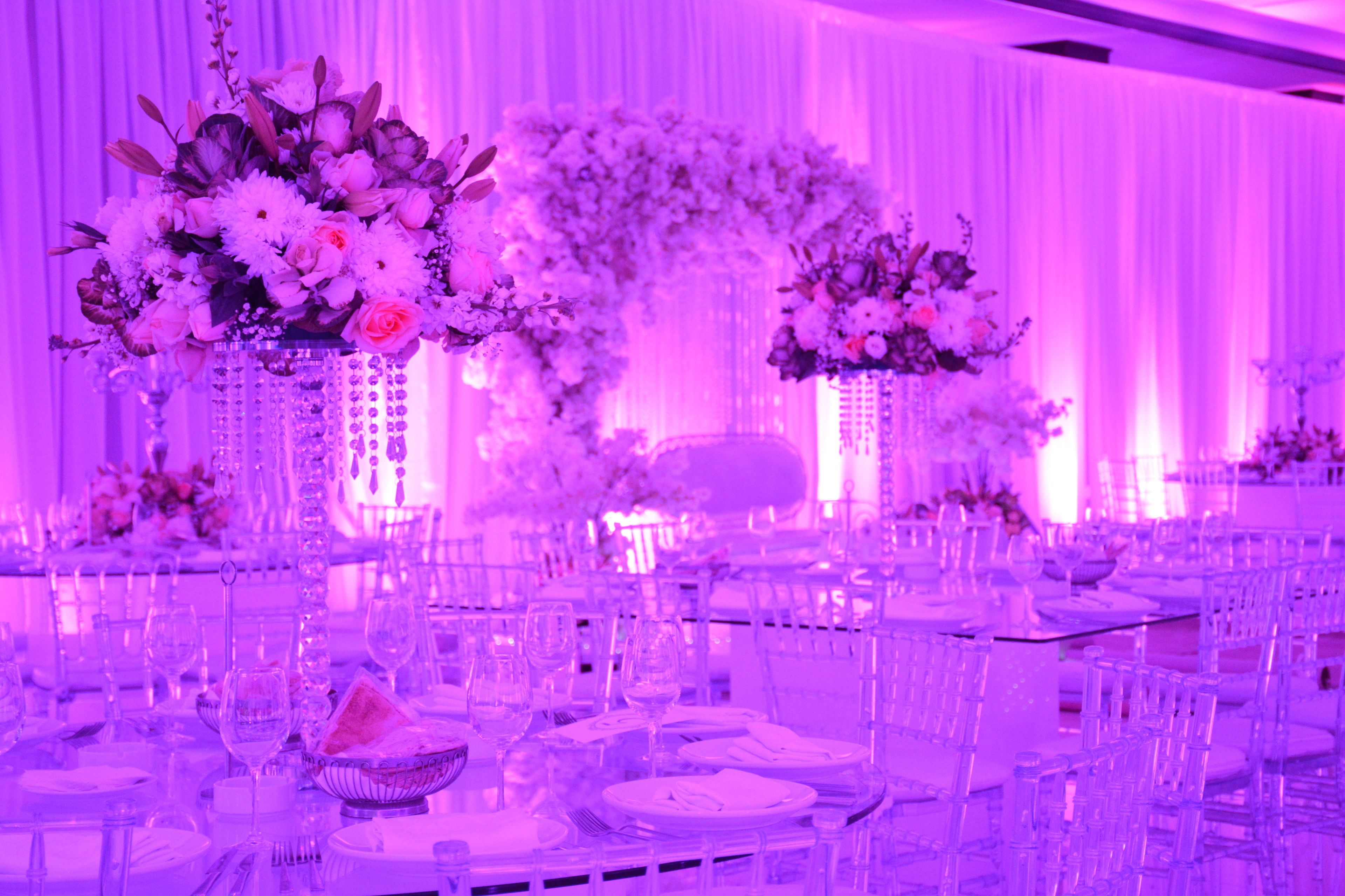 Un salón de banquetes con mesas redondas dispuestas para un evento formal, con centros de mesa florales y un telón de fondo decorado.