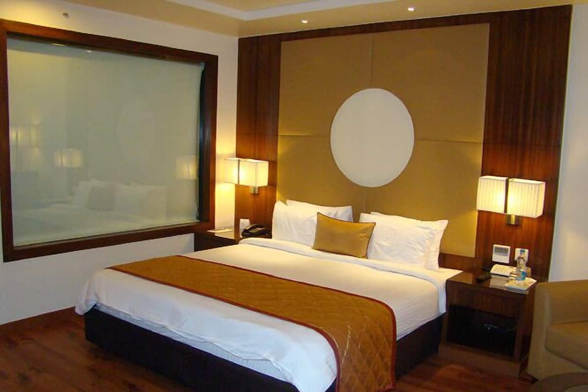 A hotel room with a large bed, wooden headboard, two bedside lamps, a nightstand, and a window with blinds.