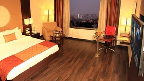 A hotel room with a large bed, a desk with a chair, a TV, and a view of a cityscape at night. - Aurick Boutique Hotel (Bengaluru)