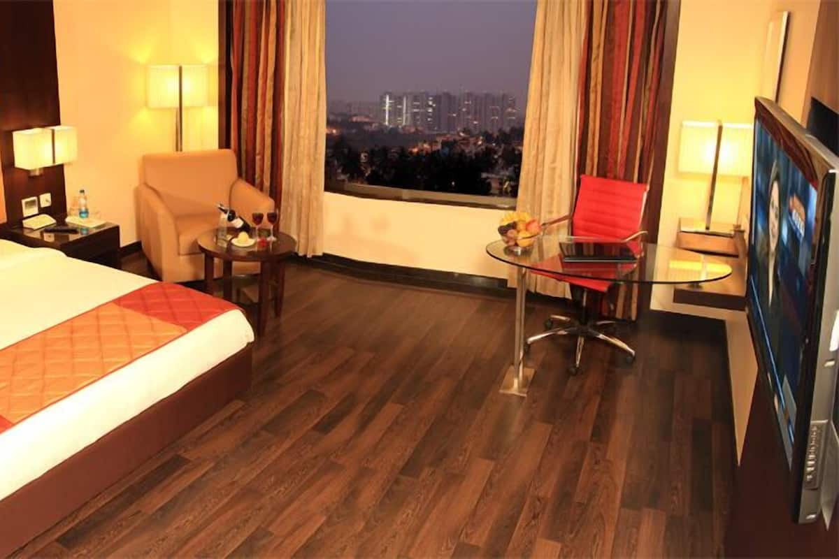A hotel room with a large bed, a desk with a chair, a TV, and a view of a cityscape at night.
