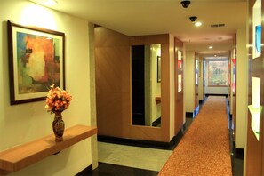 A hotel hallway with a wooden console table, a vase of flowers, a large mirror, and a carpeted floor.