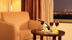 A hotel room with a sofa, a table with a bottle of wine, two glasses of wine, and a flower. - Aurick Boutique Hotel (Bengaluru)