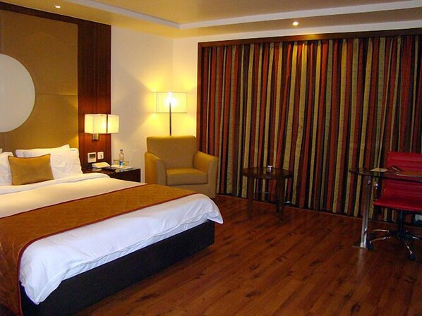 A hotel room with a large bed, two bedside lamps, a chair, a small table, and a curtain backdrop. - Aurick Boutique Hotel (Bengaluru)