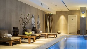 Un espace spa comprenant une piscine, des sièges et un mur où sont disposées des serviettes et une horloge.