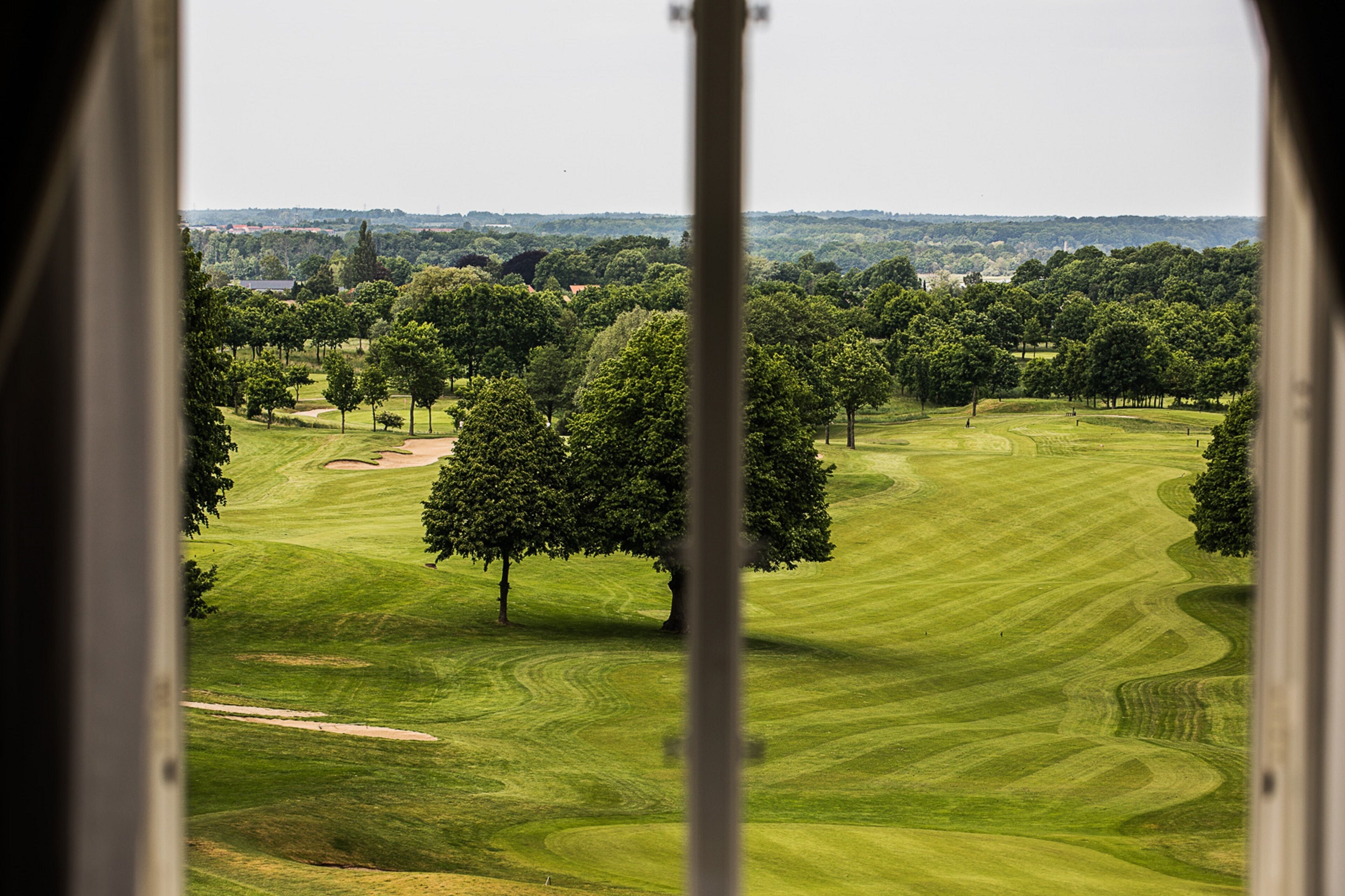 A golf course with well-manicured fairways and greens, surrounded by trees and a distant view of buildings.