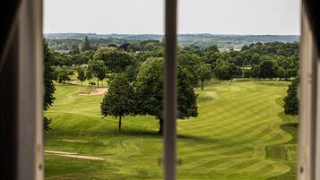 A golf course with well-manicured fairways and greens, surrounded by trees and a distant view of buildings.