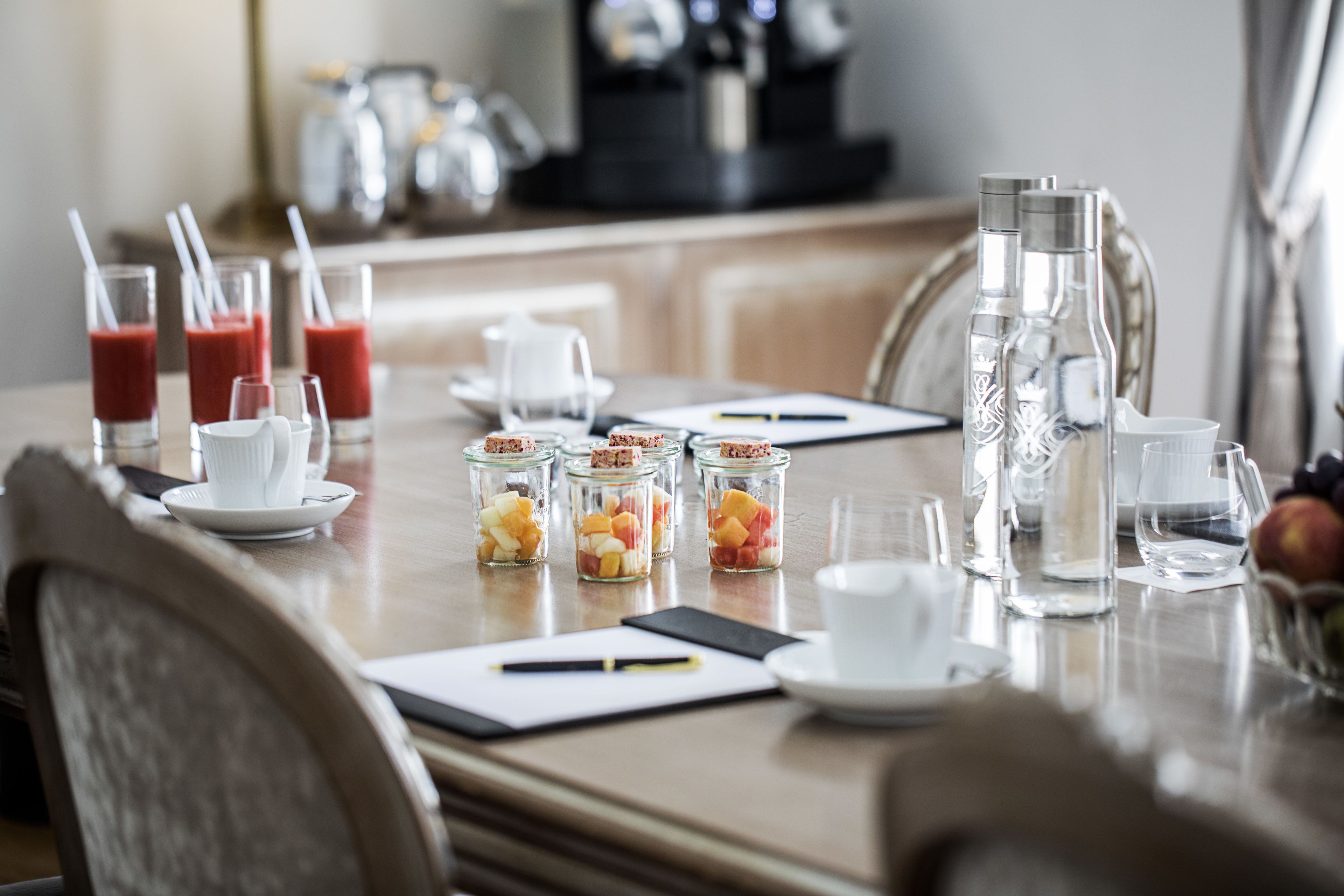 A breakfast table set with glasses of juice, a coffee maker, and fruit in jars.