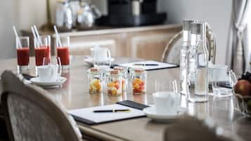 A breakfast table set with glasses of juice, a coffee maker, and fruit in jars.