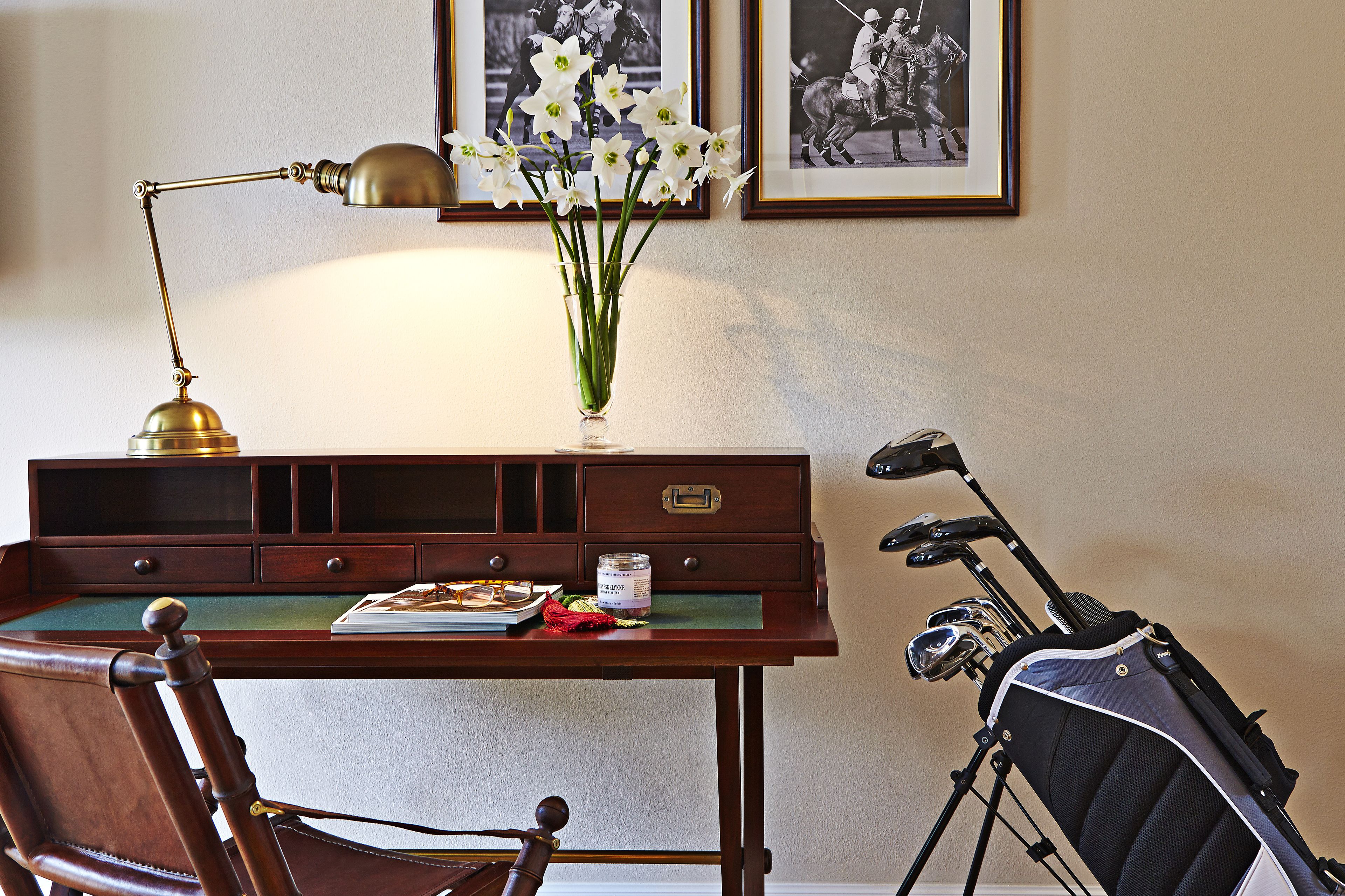 A desk with a lamp, a vase of flowers, a framed picture, and a golf bag.