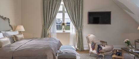 A bedroom with a large bed, a chair, a small table, and a TV mounted on the wall.