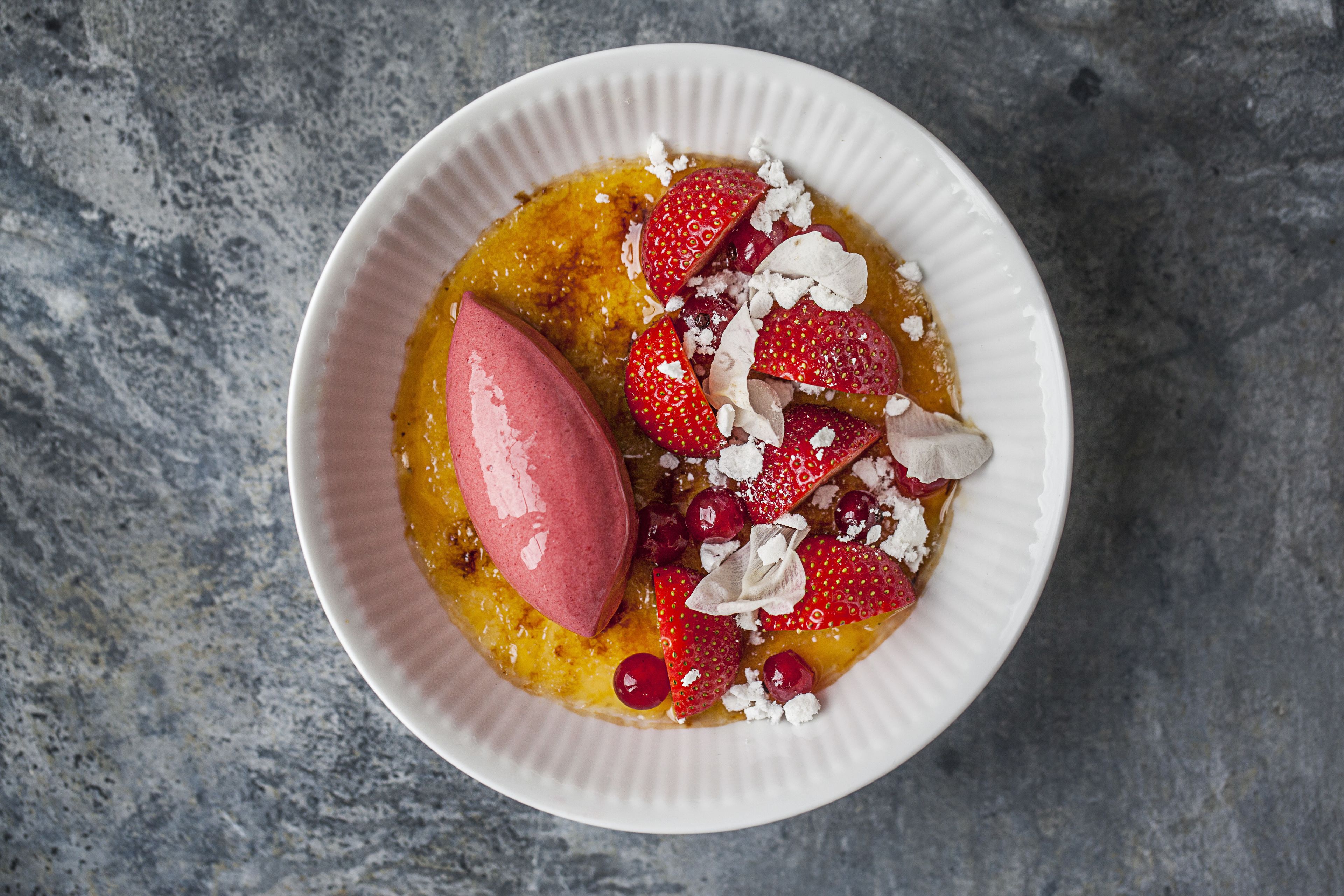 Un tazón de postre con fresas y crema sobre una superficie texturizada.
