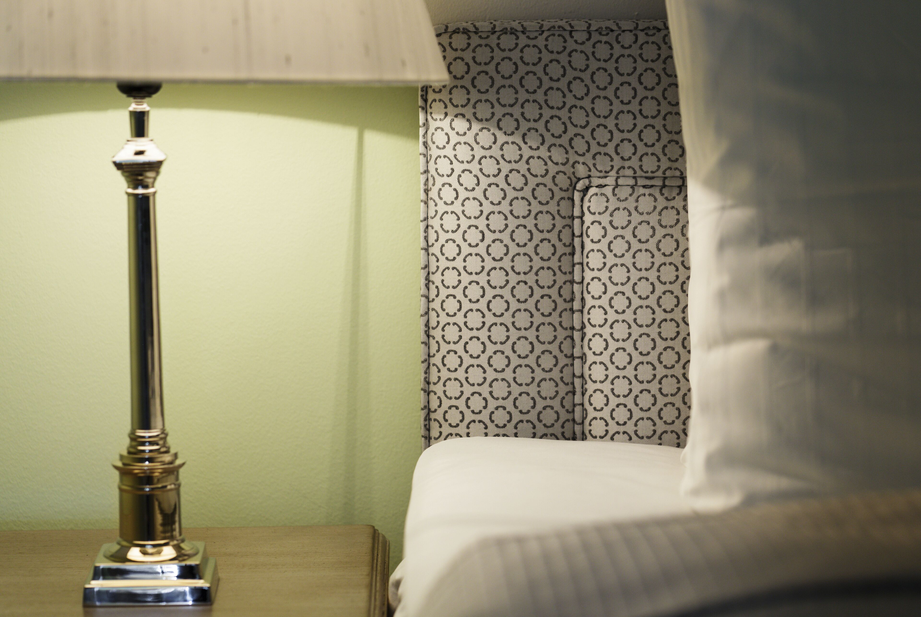 Una cama con cortinas estampadas y una lámpara de metal sobre una mesita de noche de madera.