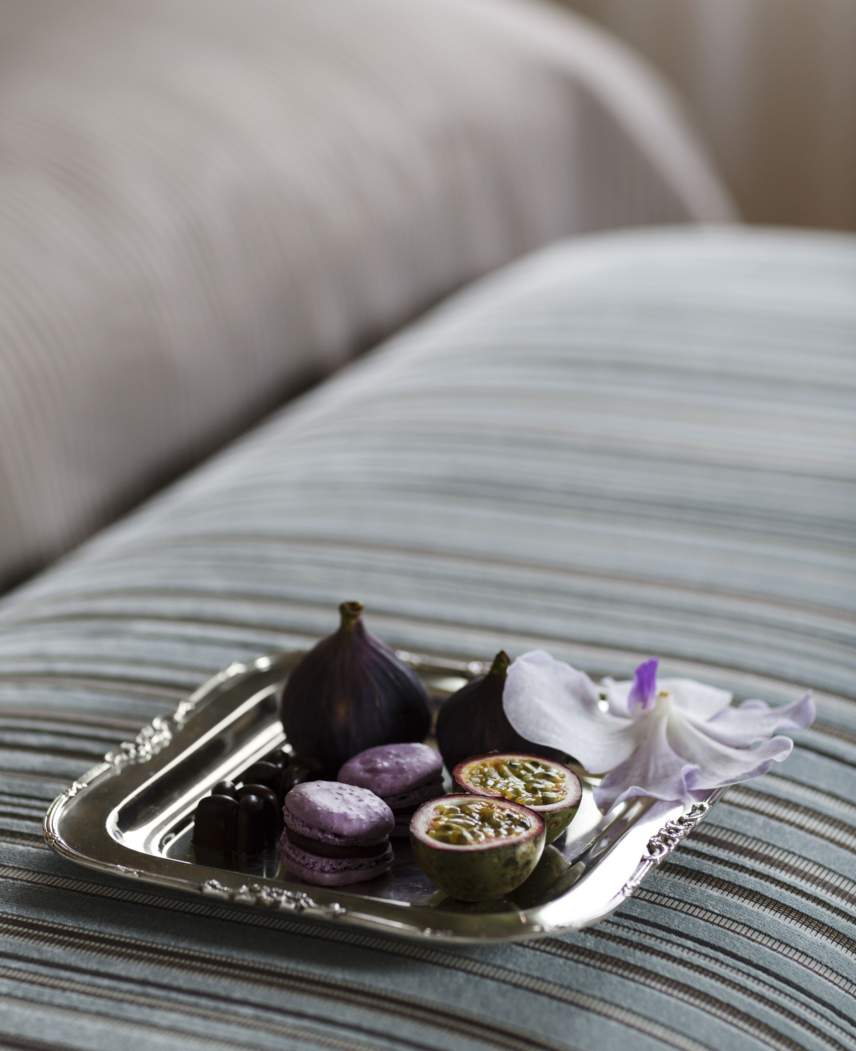 Un plateau contenant des macarons, des figues et une fleur, posé sur une surface en tissu à rayures.