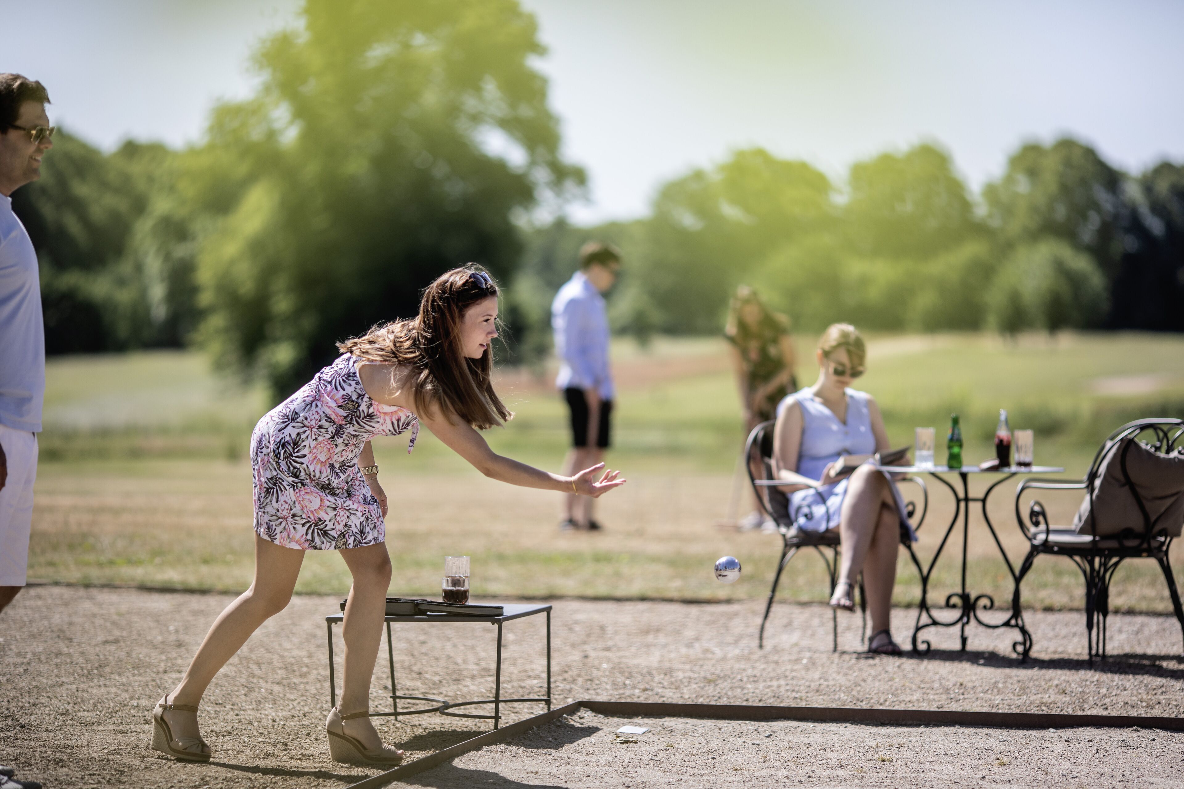 A woman playing croquet in an outdoor setting with a table and chairs in the background.