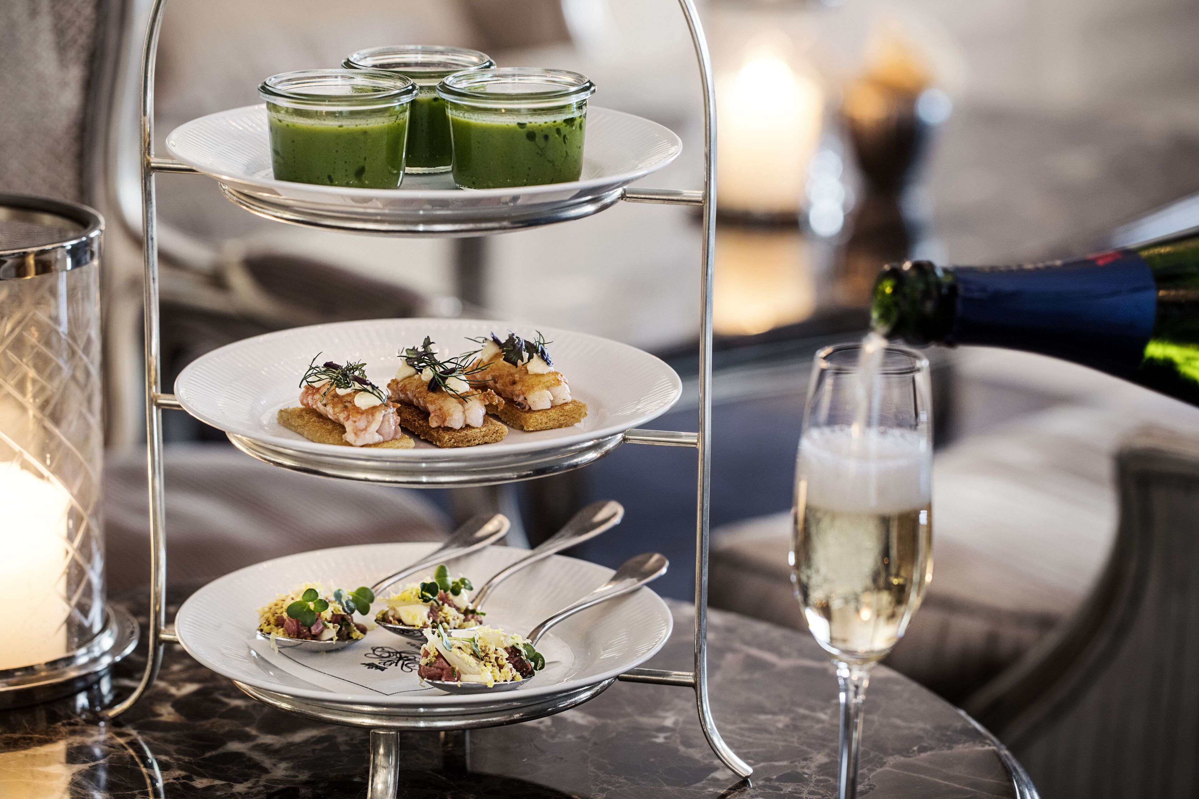 A three-tiered serving tray with various dishes and a glass of champagne on a marble table.