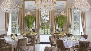 Une salle à manger élégante, dotée de lustres, de grands miroirs et offrant une vue sur l’extérieur.