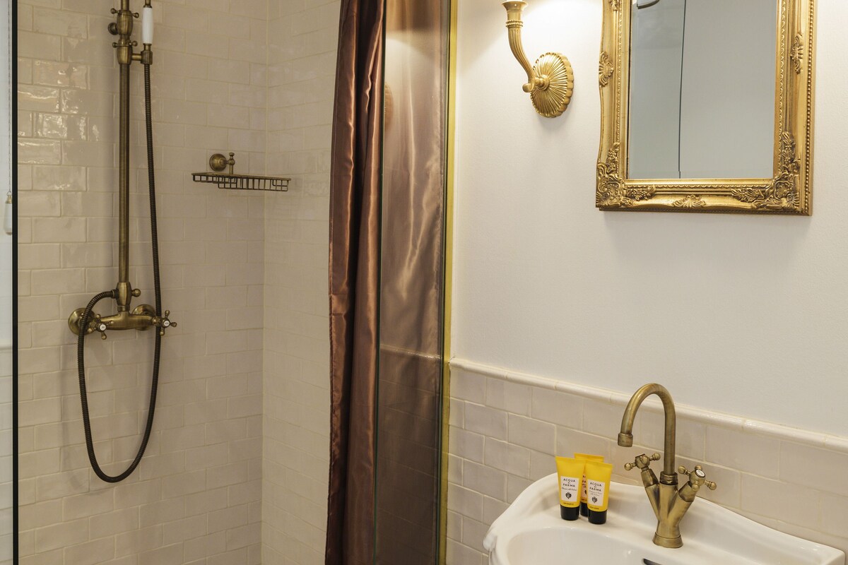 Un baño con ducha, lavamanos, espejo y una cesta de toallas.