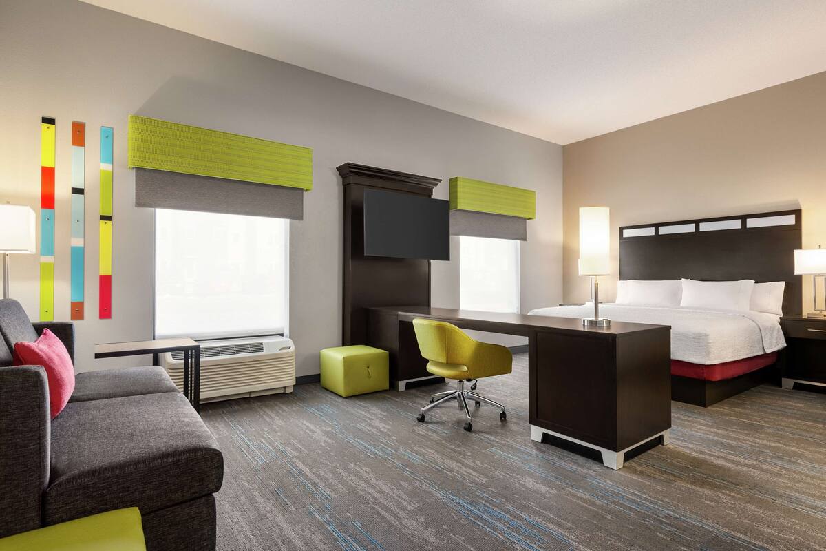 A hotel room with a bed, desk, chair, and a couch.